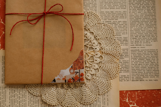 Gift wrapped in brown paper with red string on a textured surface with lace doily