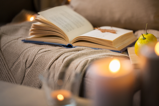 Open book on a cushion with candles and a pear in the foreground
